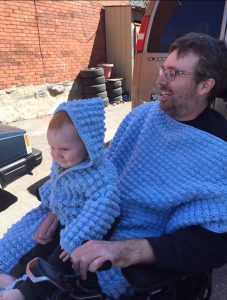 Man living with ALS holding infant son in his power wheelchair